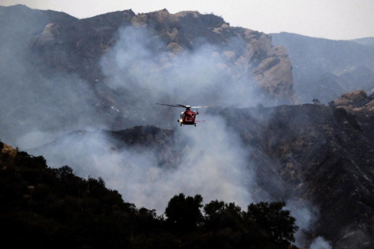 A firefighting helicopter prepares to drop water onto a wildfire in the Pacific Palisades area of Los Angeles, Sunday, May 16, 2021. (AP Photo/Ringo H.W.