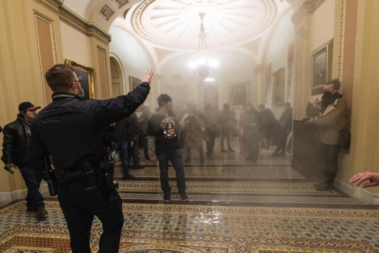 FILE - In this Jan. 6, 2021, file photo, smoke fills the walkway outside the Senate Chamber as supporters of President Donald Trump are confronted by U.S. Capitol Police officers inside the Capitol in Washington. With riot cases flooding into Washington's federal court, the Justice Department is under pressure to quickly resolve the least serious cases.