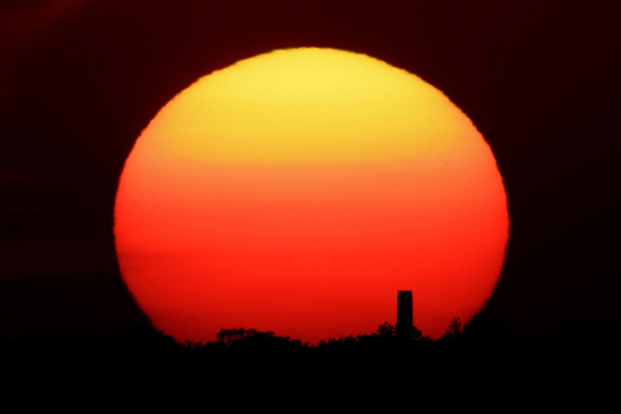 The sun sets behind a smokestack June 26 in Kansas City, Mo.