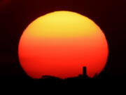 The sun sets behind a smokestack June 26 in Kansas City, Mo.