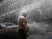 FILE - In this Tuesday, July 28, 2020 file photo, Rey Gomez cools off in the spray from a fire hydrant in New York, as the city opened more than 300 fire hydrants with sprinkler caps to help residents cool off during a heat wave. According to a study published Tuesday, May 25, 2021 in Nature Communications, during the summer of 2017 in nearly all large urban areas, people of color are exposed to more extreme urban heat than white people.