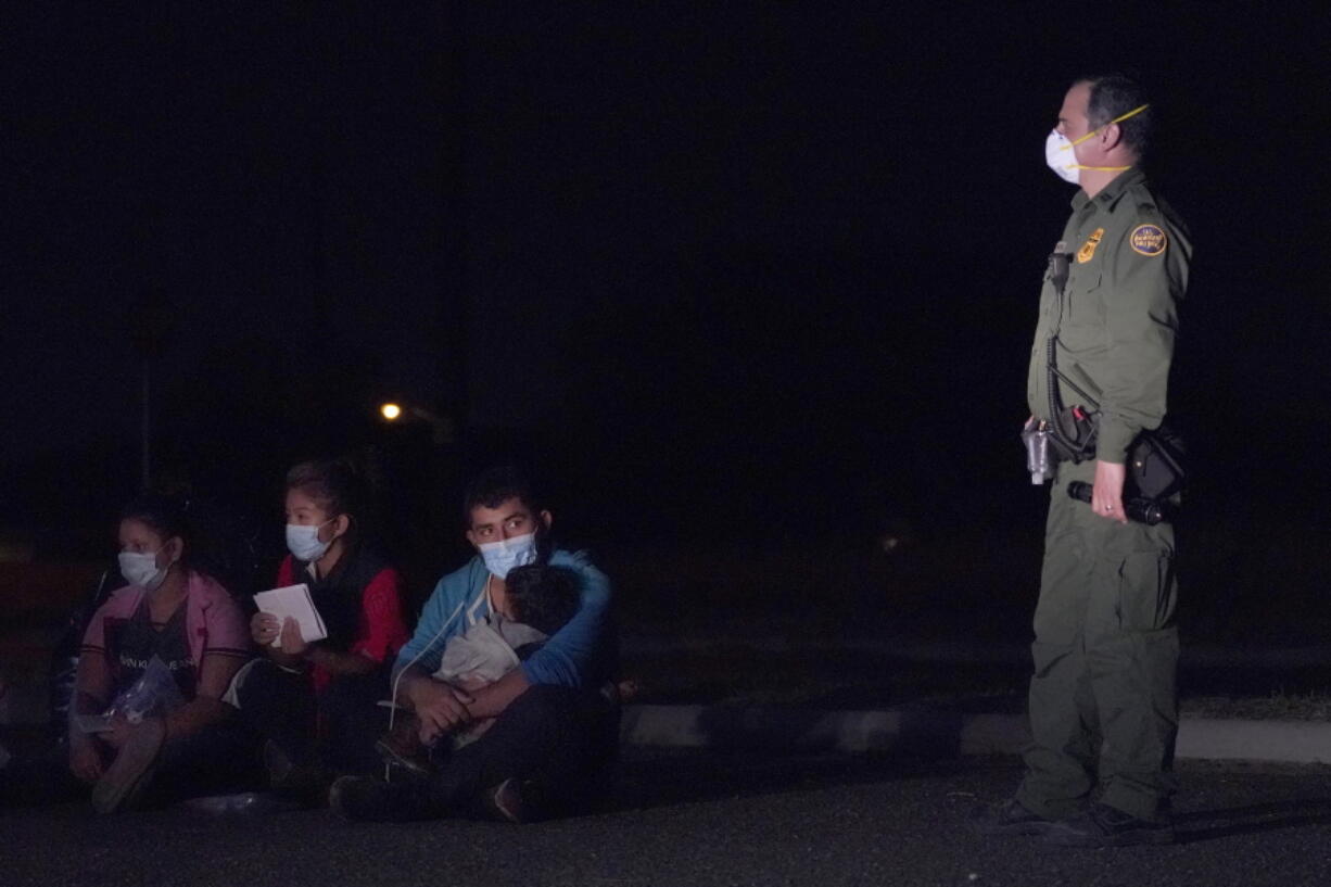 In this March 24, 2021 photo, a migrant man, center, holds a child as he looks at a U.S. Customs and Border Protection agent at an intake area after crossing the U.S.-Mexico border, early Wednesday, March 24, 2021, in Roma, Texas. The Biden administration said Monday that four families that were separated at the Mexico border during Donald Trump's presidency will be reunited in the United States this week in what Homeland Security Secretary Alejandro Mayorkas calls "just the beginning" of a broader effort.