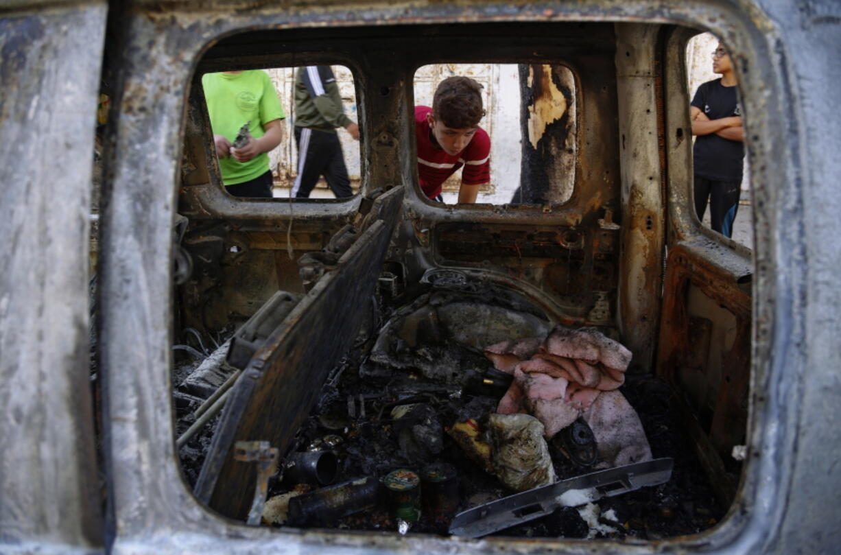 Palestinian kids look at a destroyed car after it was hit in an Israeli airstrike, in Gaza City, Wednesday, May 19, 2021.