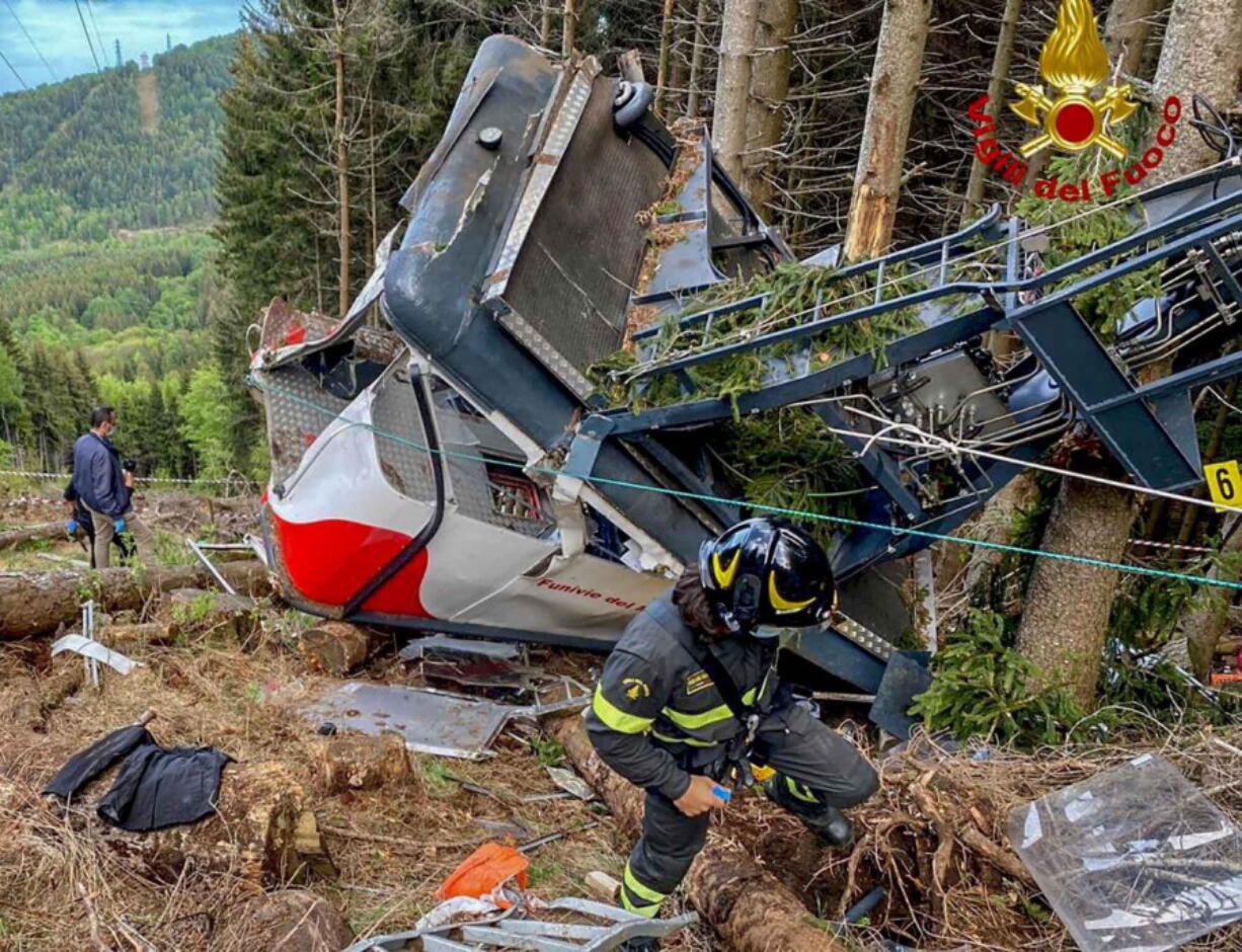 Rescuers work by the wreckage of a cable car after it collapsed near the summit of the Stresa-Mottarone line in the Piedmont region, northern Italy, Sunday, May 23, 2021. A cable car taking visitors to a mountaintop view of some of northern Italy's most picturesque lakes plummeted to the ground Sunday and then tumbled down the slope, killing at least 13 people and sending two children to the hospital, authorities said.