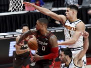 Portland Trail Blazers guard Damian Lillard, center, passes the ball behind his back to guard CJ McCollum, left, as Denver Nuggets forward Michael Porter Jr., right, defends during the first half of an NBA basketball game in Portland, Ore., Sunday, May 16, 2021.