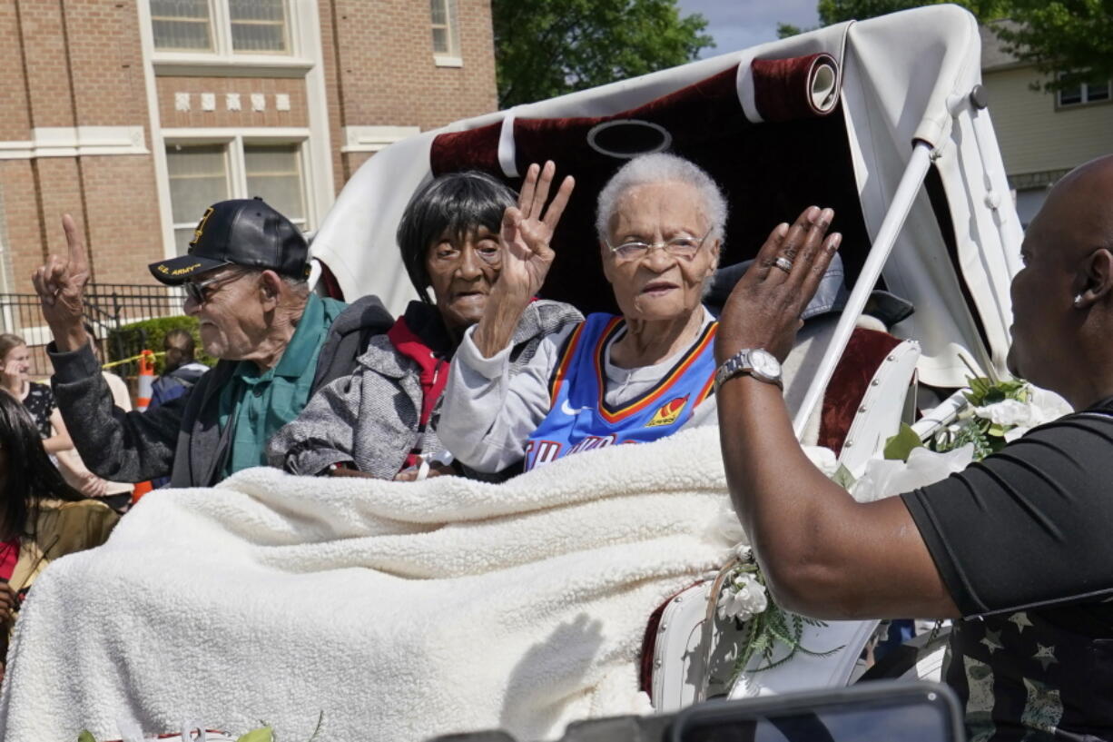 FILE - In this Friday, May 28, 2021 file photo, Tulsa Race Massacre survivors, from left, Hughes Van Ellis Sr., Lessie Benningfield Randle, and Viola Fletcher, wave and high-five supporters from a horse-drawn carriage before a march in Tulsa, Okla. Earlier in the month, the three gave testimony in a panel about the massacre in the U.S. House of Representatives.