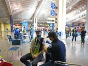 FILE - In this May 2, 2021, file photo, Austin Kennedy, left, a Seattle Sounders season ticket holder, gets the Johnson & Johnson COVID-19 vaccine at a clinic in a concourse at Lumen Field in Seattle, prior to an MLS soccer match between the Sounders and the Los Angeles Galaxy. Rising coronavirus cases and hospitalizations in Washington and Oregon have led Oregon officials to move toward further restrictions. Washington is taking a two-week pause to evaluate before making a decision.  (AP Photo/Ted S.