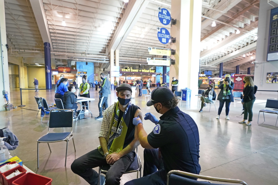 FILE - In this May 2, 2021, file photo, Austin Kennedy, left, a Seattle Sounders season ticket holder, gets the Johnson & Johnson COVID-19 vaccine at a clinic in a concourse at Lumen Field in Seattle, prior to an MLS soccer match between the Sounders and the Los Angeles Galaxy. Rising coronavirus cases and hospitalizations in Washington and Oregon have led Oregon officials to move toward further restrictions. Washington is taking a two-week pause to evaluate before making a decision.  (AP Photo/Ted S.