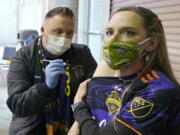 FILE - In this May 2, 2021, file photo, Stephanie Birman, right, a Seattle Sounders season ticket holder, wears a Sounders mask, jersey and earrings as she gets the Johnson & Johnson COVID-19 vaccine at a clinic in a concourse at Lumen Field prior to an MLS soccer match between the Sounders and the Los Angeles Galaxy. On Thursday, May 20, 2021, authorities in King County, Wash., which includes Seattle, said all people should continue wearing masks indoors until 70% of people in the county 16 and older are fully vaccinated. (AP Photo/Ted S.