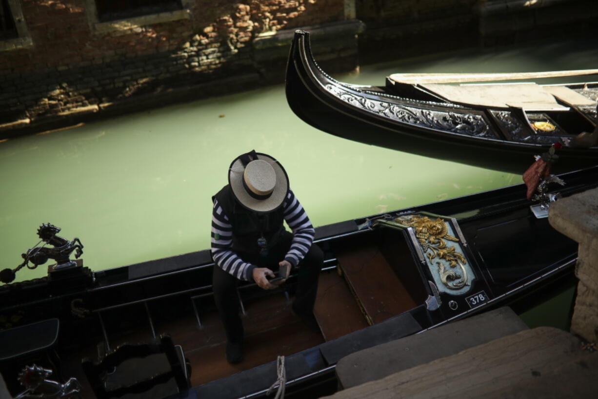 FILE - In this Friday, Feb. 28, 2020 file photo, a gondolier looks at his smartphone as he waits for clients in Venice, Italy.