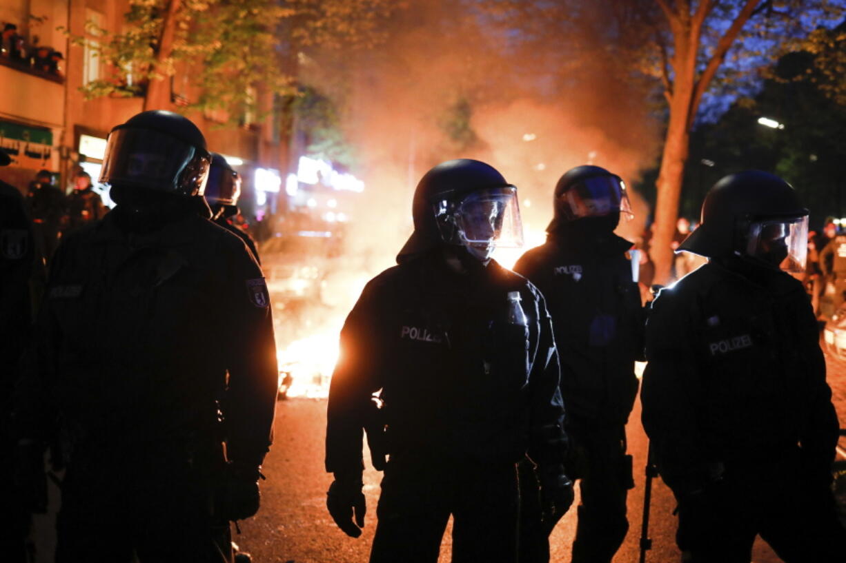 Police officers stand in front of a fire set up by demonstrators during a May Day rally in Berlin, Germany, Saturday, May 1, 2021.