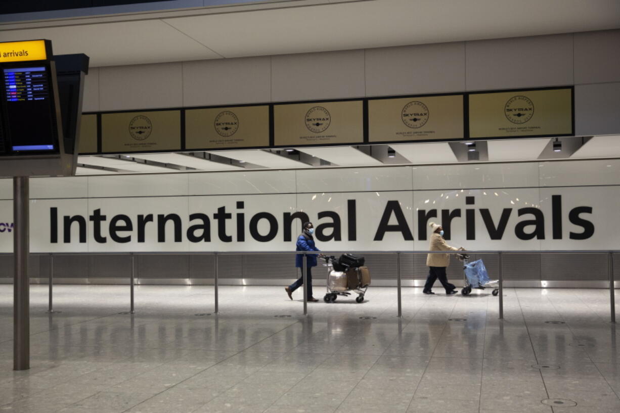 FILE - In this Tuesday, Jan. 26, 2021 file photo, arriving passengers walk past a sign in the arrivals area at Heathrow Airport in London, during England's third national lockdown since the coronavirus outbreak began. Keen to avoid losing another summer of holiday revenue to the coronavirus pandemic, the European Union, some Asian governments and the airline industry are scrambling to develop so-called COVID-19 vaccine passports to help kickstart international travel.