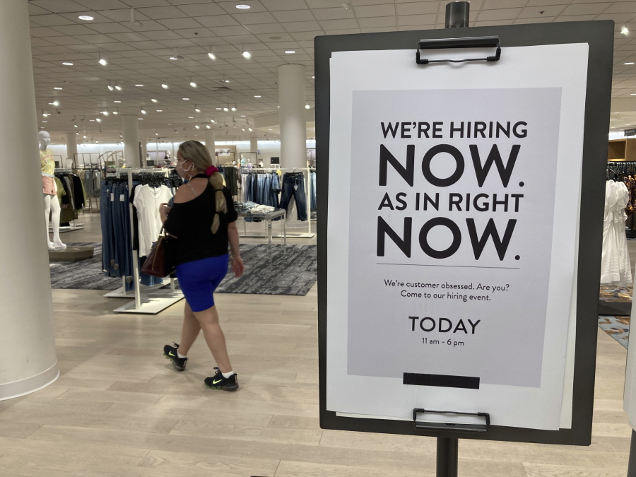 A customer walks behind a sign at a Nordstrom store seeking employees, Friday, May 21, 2021, in Coral Gables, Fla.  The number of Americans seeking unemployment benefits dropped last week to 406,000, a new pandemic low and more evidence that the job market is strengthening as the virus wanes and economy further reopens.