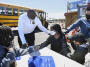 FILE - In this April 26, 2021, file photo, East Hartford High School senior Sudeen Pryce, right, center, receives support from classmate Alexia Phipps, left, East Hartford High School Intervention Coordinator Mark Brown, second from left, and EMT Katrinna Greene, top right, of Manchester, as RN Kaylee Cruz of Bristol administers the first dose of the Pfizer vaccine to Pryce at a mass vaccination site at Pratt & Whitney Runway in East Hartford, Conn.