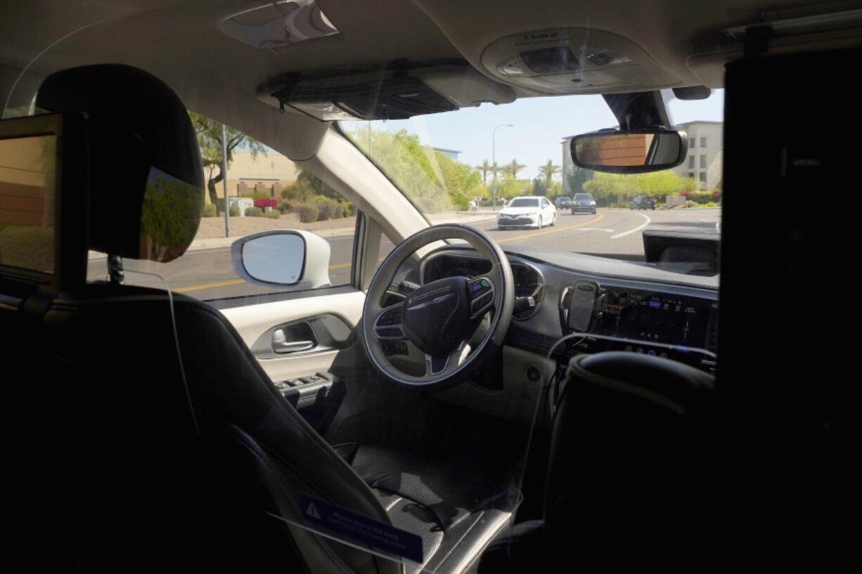 A Waymo minivan moves along a city street as an empty driver's seat and a moving steering wheel drive passengers during an autonomous vehicle ride, Wednesday, April 7, 2021, in Chandler, Ariz.  Waymo, a unit of Google parent Alphabet Inc., is one of several companies testing driverless vehicles in the U.S. But it's the first offering lifts to the public with no humans at the wheel who can take over in sticky situations. (AP Photo/Ross D. Franklin) (Ross D.