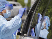 Medical assistant Melanie Zamudio is reflected in the window of a car as she reaches in to take a nasal swab from a driver at a drive-up coronavirus testing site in April 2020 in Seattle.