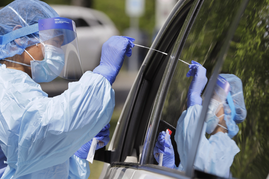 Medical assistant Melanie Zamudio is reflected in the window of a car as she reaches in to take a nasal swab from a driver at a drive-up coronavirus testing site in April 2020 in Seattle.