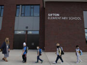 Kindergarten teacher Katie Plamondon, from left, leads students Phoenix Winmil, 5, Wes Charuchinda, 5, Emery Thomas, 6, and Jay Chou, 6, into the building for their second day of classes at Sifton Elementary School last Sept. 22. Smaller districts are exploring permanent remote options for families who choose them.