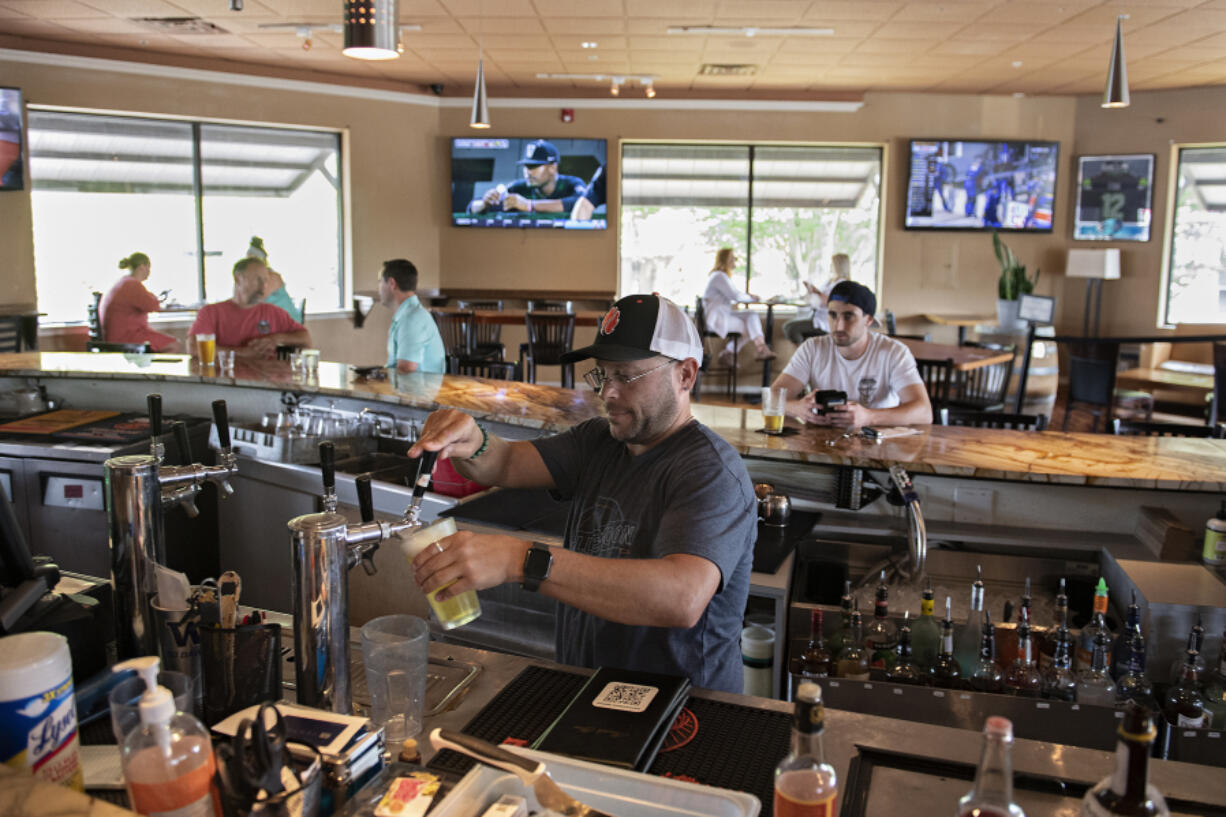 Bartender Mike Dunning of Main Event Sports Grill in east Vancouver pours drinks for customers while working behind the bar on Wednesday afternoon. Statewide pandemic restrictions ended on Wednesday, allowing restaurants and bars to reopen their bar counter seating areas for the first time in more than a year.