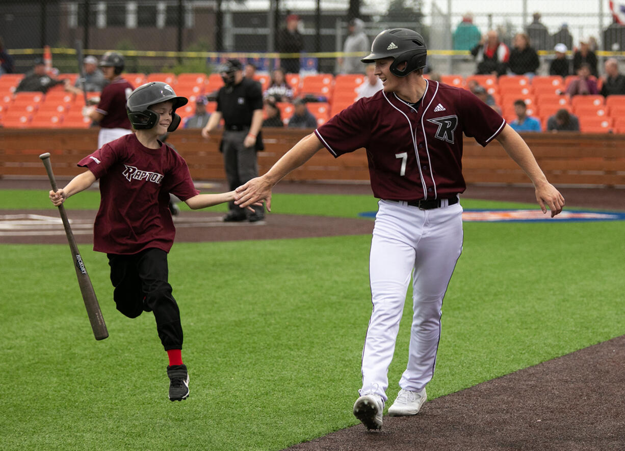 Ridgefield's Caden Connor (7) celebrates with bat boy Colton Schreiber, 9, of Battleground, after scoring a run against Bellingham during the second inning of a West Coast League baseball game  at the Ridgefield Outdoor Recreation Complex on Wednesday, June 30, 2021.