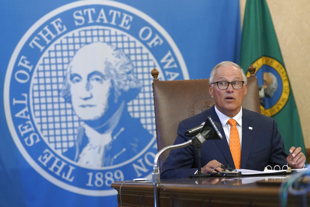 Washington Gov. Jay Inslee glances at an aide holding up an image of a visual slide being shown to viewers of a news conference, Thursday, June 3, 2021, in Olympia, Wash. Inslee announced that Washington will be the latest state to offer prizes to encourage people to get vaccinated against COVID-19. Incentives will include a series of giveaways during the month of June including lottery prizes totaling $2 million, college tuition assistance, airline tickets, and game systems. (AP Photo/Ted S.