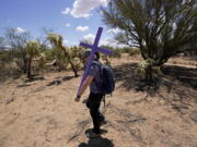 Alyssa Quintanilla, part of the Tucson Samaritans volunteer group, carries a cross May 18 to be installed at the site of the migrant who died in the desert some time ago in the desert near Three Points, Ariz. (Photos by Ross D.