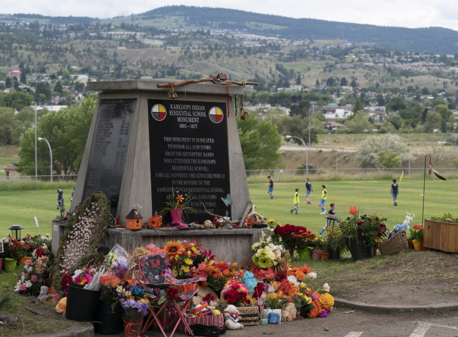 Children play soccer in the background as a memorial is pictured outside the Residential School in Kamloops, British Columbia., Sunday, June, 13, 2021. The remains of 215 children were discovered buried near the former Kamloops Indian Residential School earlier this month.