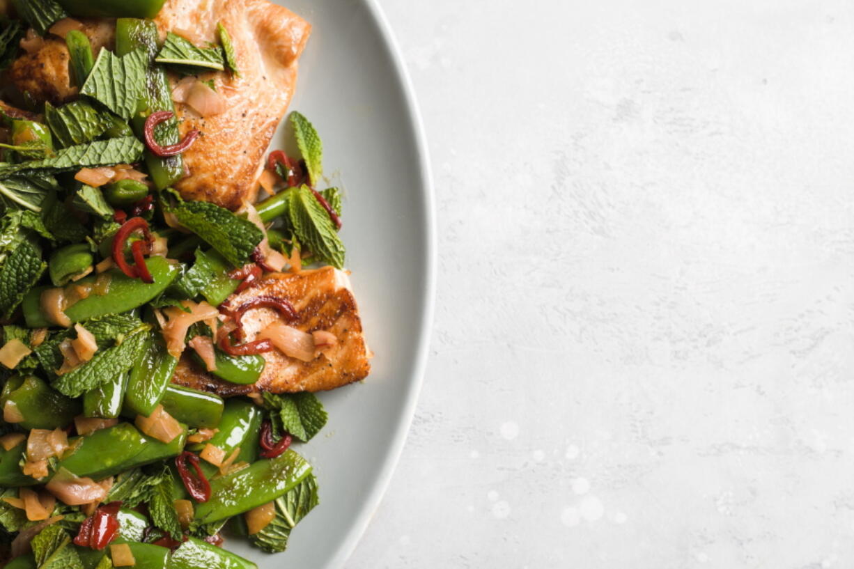 This image released by Milk Street shows a recipe for salmon with chilies, pickled ginger and snap peas.