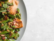 This image released by Milk Street shows a recipe for salmon with chilies, pickled ginger and snap peas.