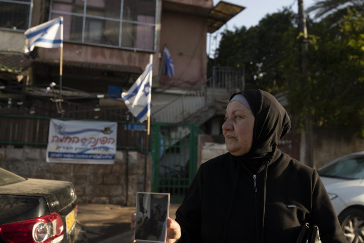 Maryam Ghawi, a Palestinian, holds a family photo taken in the home behind her that is now occupied by Israeli settlers in the Sheikh Jarrah neighborhood of east Jerusalem, where hers is among dozens of Palestinian families facing imminent eviction from their homes by Israeli settlers, Tuesday, May 25, 2021.  After weeks of unrest that captured international attention, the evictions could still proceed.