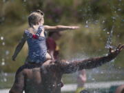 Keeping cool in record setting temperatures, Beau Jess and daughter River, 3, reach for falling water as they play at the Splash Pad in Haller Park on Monday, June 28, 2021 in Arlington, Wash.