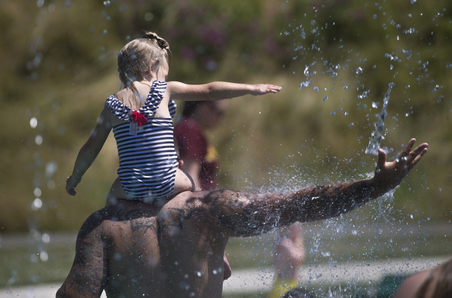 Keeping cool in record setting temperatures, Beau Jess and daughter River, 3, reach for falling water as they play at the Splash Pad in Haller Park on Monday, June 28, 2021 in Arlington, Wash.