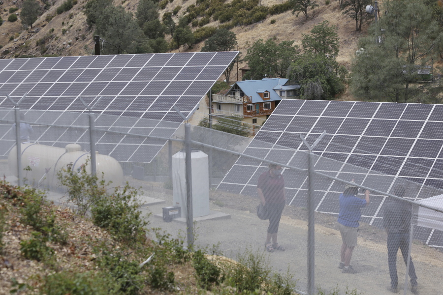 A house shown in the distance is powered by Pacific Gas & Electric's new Remote Grid Initiative site shown near Yosemite National Park in Briceburg, Calif., on June 7, 2021. When a wildfire tore through Briceburg nearly two years earlier, the tiny community on the edge of Yosemite National Park lost the only power line connecting it to the electrical grid. Rather than rebuilding poles and wires over increasingly dry hillsides, which could increase the risk of equipment igniting catastrophic fires, the nation's largest utility decided to give Briceburg a self-reliant power system.