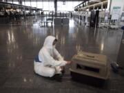 FILE - In this Thursday, April 2, 2020 file photo, a traveler wearing a hazmat suit tends to his dog in a carrier before boarding a plane at the Narita International Airport in Nairta, near Tokyo. U.S. health officials are planning to temporarily ban importation of dogs from more than 100 countries that are considered at high risk for rabies, planned to go into effect on July 14, 2021. Japan is not included in the ban. (AP Photo/Jae C.