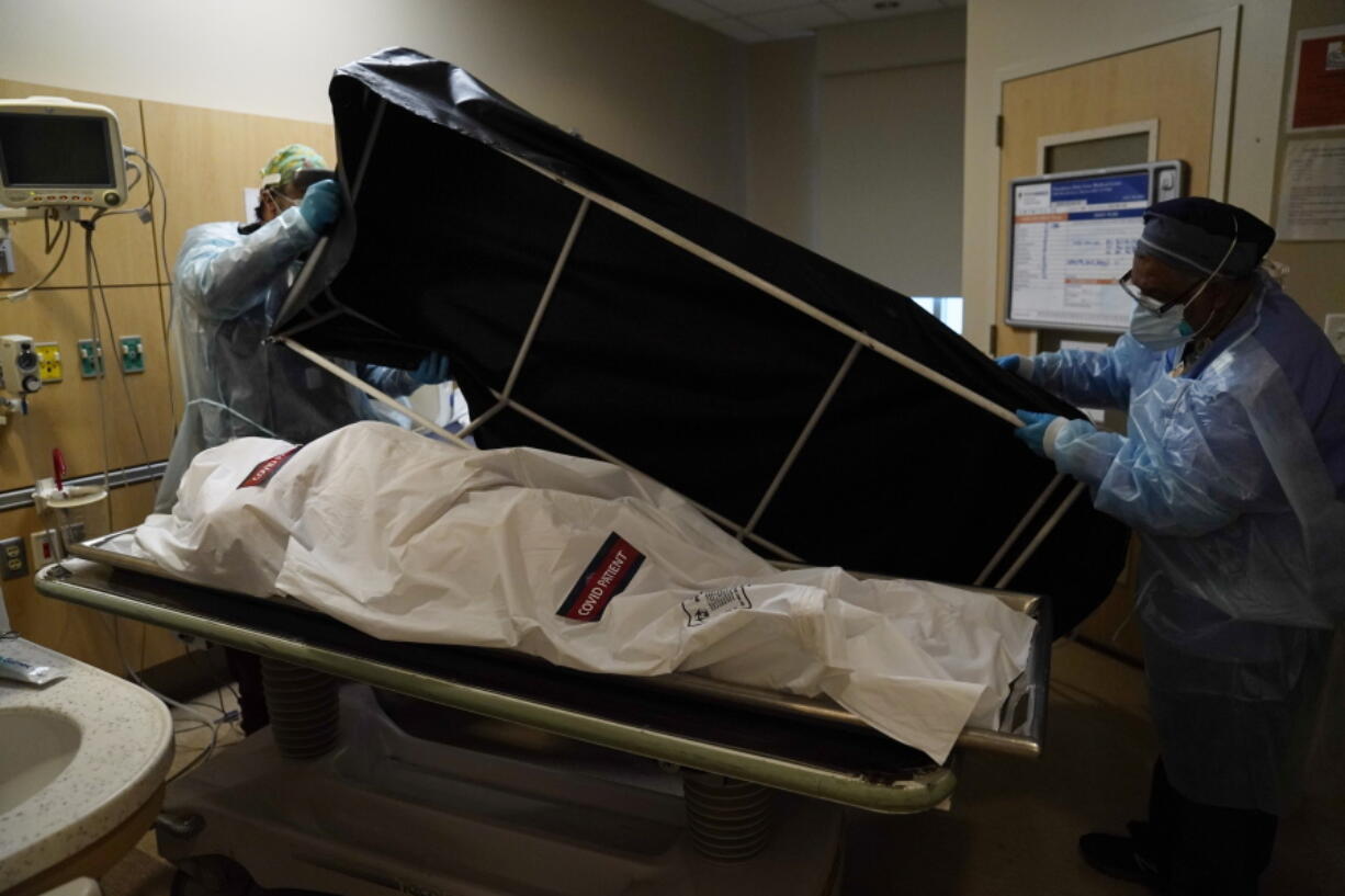 FILE - In this Jan. 9, 2021 file photo, transporters Miguel Lopez, right, Noe Meza prepare to move a body of a COVID-19 victim to a morgue at Providence Holy Cross Medical Center in the Mission Hills section of Los Angeles. The U.S. death toll from COVID-19 has topped 600,000, even as the vaccination drive has drastically slashed daily cases and deaths and allowed the country to emerge from the gloom. (AP Photo/Jae C.