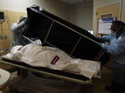 FILE - In this Jan. 9, 2021 file photo, transporters Miguel Lopez, right, Noe Meza prepare to move a body of a COVID-19 victim to a morgue at Providence Holy Cross Medical Center in the Mission Hills section of Los Angeles. The U.S. death toll from COVID-19 has topped 600,000, even as the vaccination drive has drastically slashed daily cases and deaths and allowed the country to emerge from the gloom. (AP Photo/Jae C.