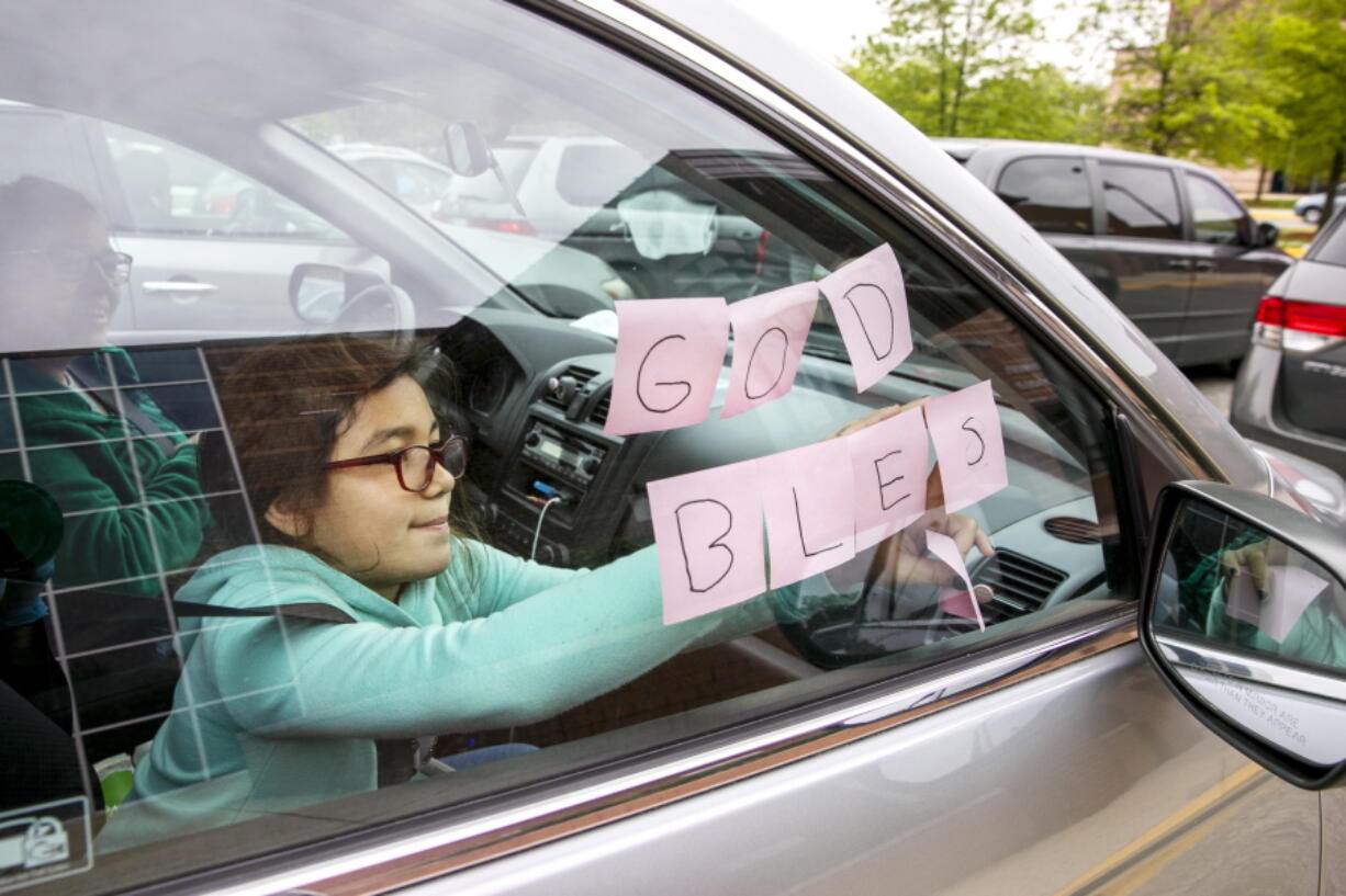 FILE - In this May 5, 2020, file photo, Elizabeth Ruiz, 7, puts up post-it notes on her mother's car window that spell out "God Bless U" as she and her mother Daylin Lemus, of Adelphi, Md., wait in a line of hundreds of cars to receive a Catholic Charities distribution of food at Northwestern High School, in Hyattsville, Md. The Department of Agriculture is sending $1 billion to the country's food bank networks, seeking to expand the reach of the system and revamp the way food banks acquire and distribute aid.