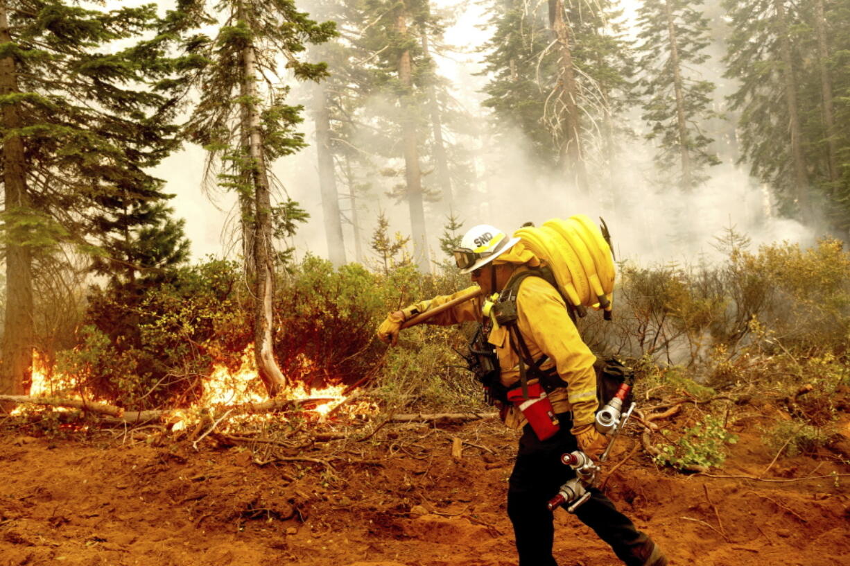 FILE - In this Sept. 14, 2020 file photo Cal Fire Battalion Chief Craig Newell carries a hose while battling the North Complex Fire in Plumas National Forest, Calif. U.S. wildfire managers are considering shifting from seasonal firefighting crews to full-time, year-round crews to deal with what has become a year-round wildfire season and to make wildland firefighting jobs more attractive by increasing pay and benefits. U.S. Forest Service Deputy Chief Christopher French, testifying before the U.S. Senate Committee on Energy and Natural Resources, said Thursday, June 24, 2021 agencies will seek to convert at least 1,000 seasonal wildland firefighters to permanent, full-time, year-round workers.