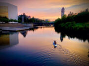 An unidentified paddler, who had slipped under the safety cables above the Upper Falls Dam moments earlier, glides past the Spokane Convention Center and toward the Riverfront Park clock tower on July 18, just after sunset. Because of nearby dams, spillways and water intakes, boating is not allowed in this area, which is controlled by Avista for its hydropower projects and public safety.