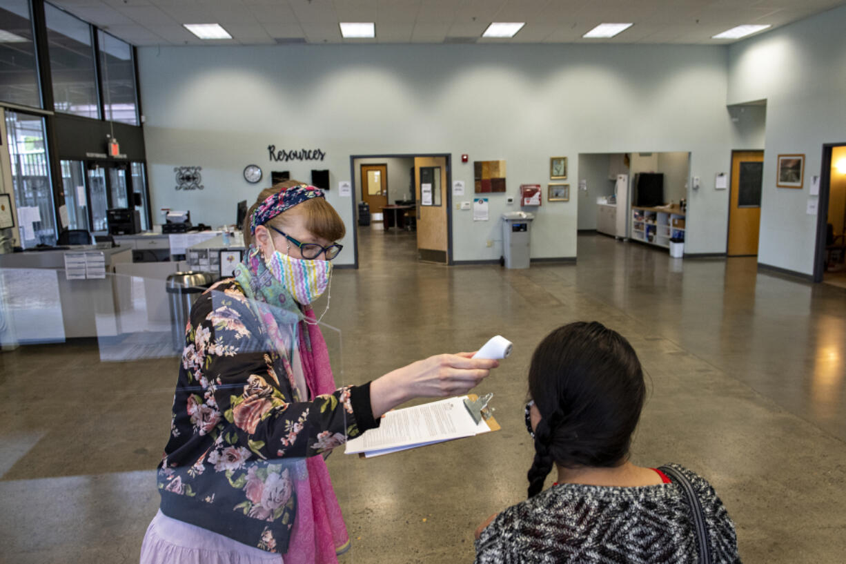 Rachel Korf, left, behavioral health receptionist for SeaMar Community Health Centers, takes the temperature of Prisli Maldonado, maternity support and community health worker, as she checks in for work at the former location of the Vancouver Navigation Center on Thursday morning, July 8, 2021.