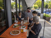 Thea Coleman of Portland, from left, looks on as server Bethany Fischer serves up lunch while joined by Isabella Coleman, 15, and Mea Agee of Vancouver while dining outside at Rally Pizza on Friday afternoon. The dining room is now also open for customers.