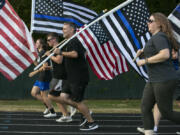 Jason Hattrick, center, CEO of Kindness 911 and organizer of the "Honor Mile" event to memorialize Detective Jeremy Brown, runs alongside other flag holders at Alki Middle School on Wednesday. Brown, a 15-year veteran of the sheriff's office, was shot and killed in the line of duty in east Vancouver Friday night.