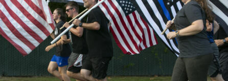 Jason Hattrick, center, CEO of Kindness 911 and organizer of the "Honor Mile" event to memorialize Detective Jeremy Brown, runs alongside other flag holders at Alki Middle School on Wednesday. Brown, a 15-year veteran of the sheriff's office, was shot and killed in the line of duty in east Vancouver Friday night.