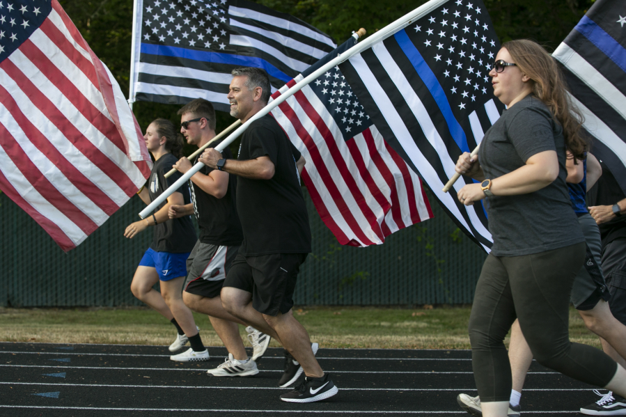 Jason Hattrick, center, CEO of Kindness 911 and organizer of the "Honor Mile" event to memorialize Detective Jeremy Brown, runs alongside other flag holders at Alki Middle School on Wednesday. Brown, a 15-year veteran of the sheriff's office, was shot and killed in the line of duty in east Vancouver Friday night.