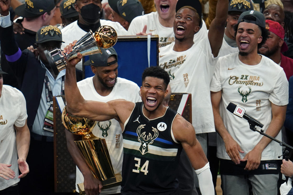 Milwaukee Bucks forward Giannis Antetokounmpo (34) reads with the championship trophy after defeating the Phoenix Suns in Game 6 of basketball's NBA Finals in Milwaukee, Tuesday, July 20, 2021. The Bucks won 105-98.