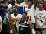 Milwaukee Bucks forward Giannis Antetokounmpo (34) reads with the championship trophy after defeating the Phoenix Suns in Game 6 of basketball's NBA Finals in Milwaukee, Tuesday, July 20, 2021. The Bucks won 105-98.