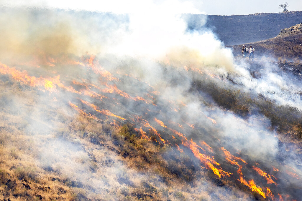 People stand behind the fire line as the flames spread through dry grasses at the Steptoe Canyon Fire  Thursday, July 22, 2021 in Colton, Wash.