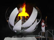 Naomi Osaka stands beside the Olympic flame after lighting it during the opening ceremony in the Olympic Stadium at the 2020 Summer Olympics, Friday, July 23, 2021, in Tokyo, Japan. (AP Photo/David J.