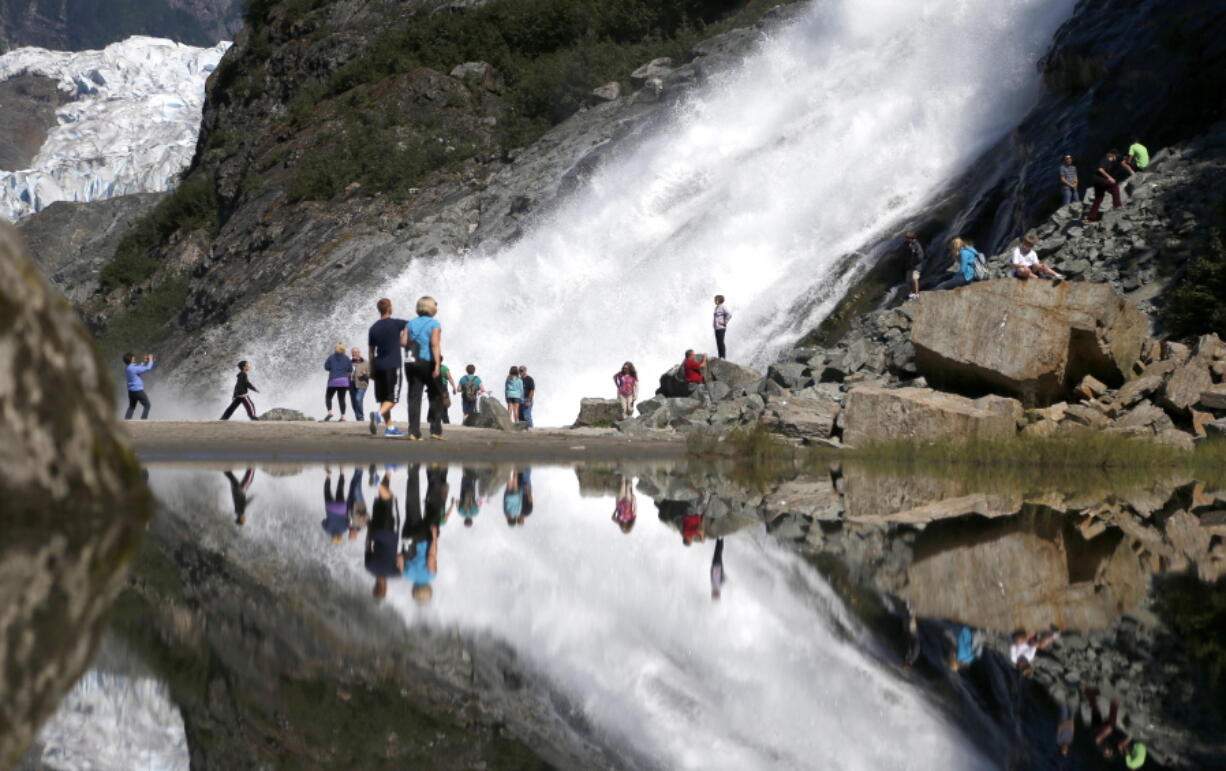 FILE - In this July 31, 2013, file photo, tourists visiting the Mendenhall Glacier in the Tongass National Forest are reflected in a pool of water as they make their way to Nugget Falls in Juneau, Alaska. The Biden administration said Thursday, July 15, 2021, that it is ending large-scale, old-growth timber sales on the nation's largest national forest, the Tongass National Forest in Alaska, and will instead focus on forest restoration, recreation and other non-commercial uses.