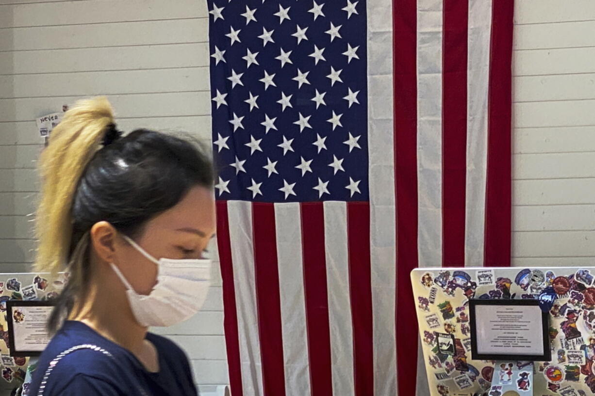 A woman wearing a face mask walks by a counter displaying an American flag at a fashion boutique in Beijing, Sunday, July 11, 2021. China on Sunday said it will take "necessary measures" to respond to the U.S. blacklisting of Chinese companies over their alleged role in abuses of Uyghur people and other Muslim ethnic minorities.